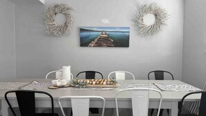 A dining area with a table set for four, featuring a painting of a pier, two decorative wreaths, and a centerpiece of eggs and greenery. - Cute 4 bed 2.5 bath Home - Sleeps 12! 30 night min (Virginia Beach)