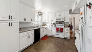 A modern kitchen with white cabinets, a granite countertop, a red rug, and a built-in oven. - Cute 4 bed 2.5 bath Home - Sleeps 12! 30 night min (Virginia Beach)