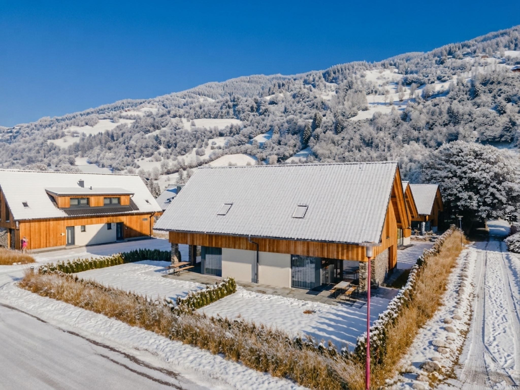 Un edificio moderno con techo inclinado, rodeado de campos y árboles cubiertos de nieve, bajo un cielo despejado.