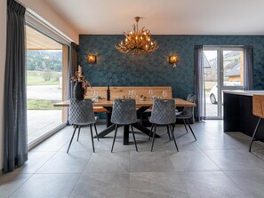 A dining area with a wooden table, grey upholstered chairs, a chandelier, and a view of the outdoors.