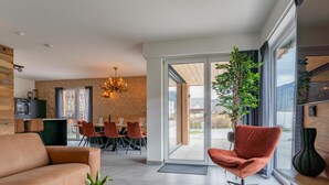 A modern living room with a sofa, a coffee table, and a dining area with chairs and a chandelier.