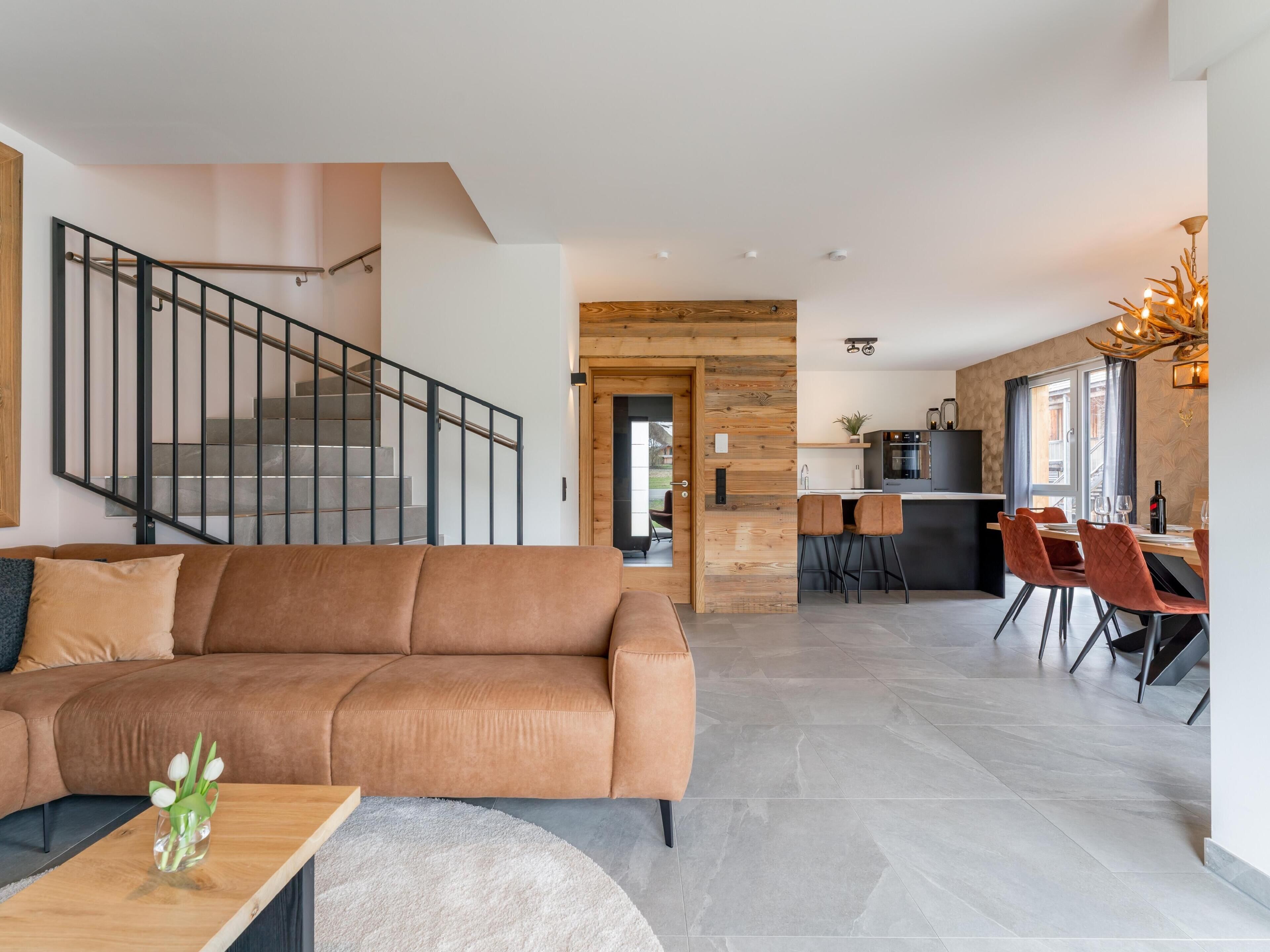 A modern living room with a brown sofa, a wooden coffee table, and a staircase.