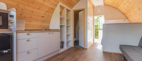 A compact kitchen with wooden walls, a built-in oven, and a grey sofa in a cozy, open-plan living area.