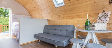 A cozy room with a grey sofa, a small round table with a bottle and glasses, and a wicker basket.