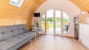 Een knus interieur van een chalet met een bank, een kleine tafel met stoelen, een televisie en een groot raam.