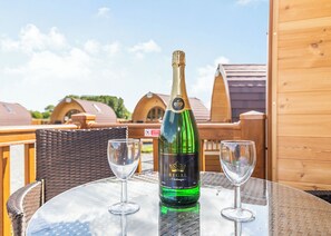 Une bouteille de champagne sur une table, accompagnée de deux verres, le tout sur fond de cabanes en bois.