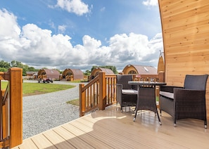 Une terrasse en bois avec des meubles d’extérieur, un chemin de gravier et, au fond, plusieurs cabanes dotées de toits en bois.