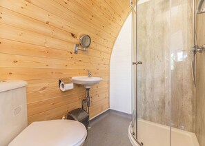 Une salle de bain aux murs lambrissés, équipée de toilettes, d’un lavabo et d’une douche à parois de verre.