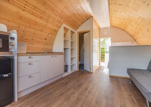 A compact kitchen with wooden walls, a built-in oven, and a grey sofa in a cozy, open-plan living area.