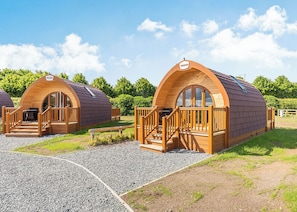 Two wooden dome-shaped cabins with wooden railings and steps, surrounded by gravel and grass.