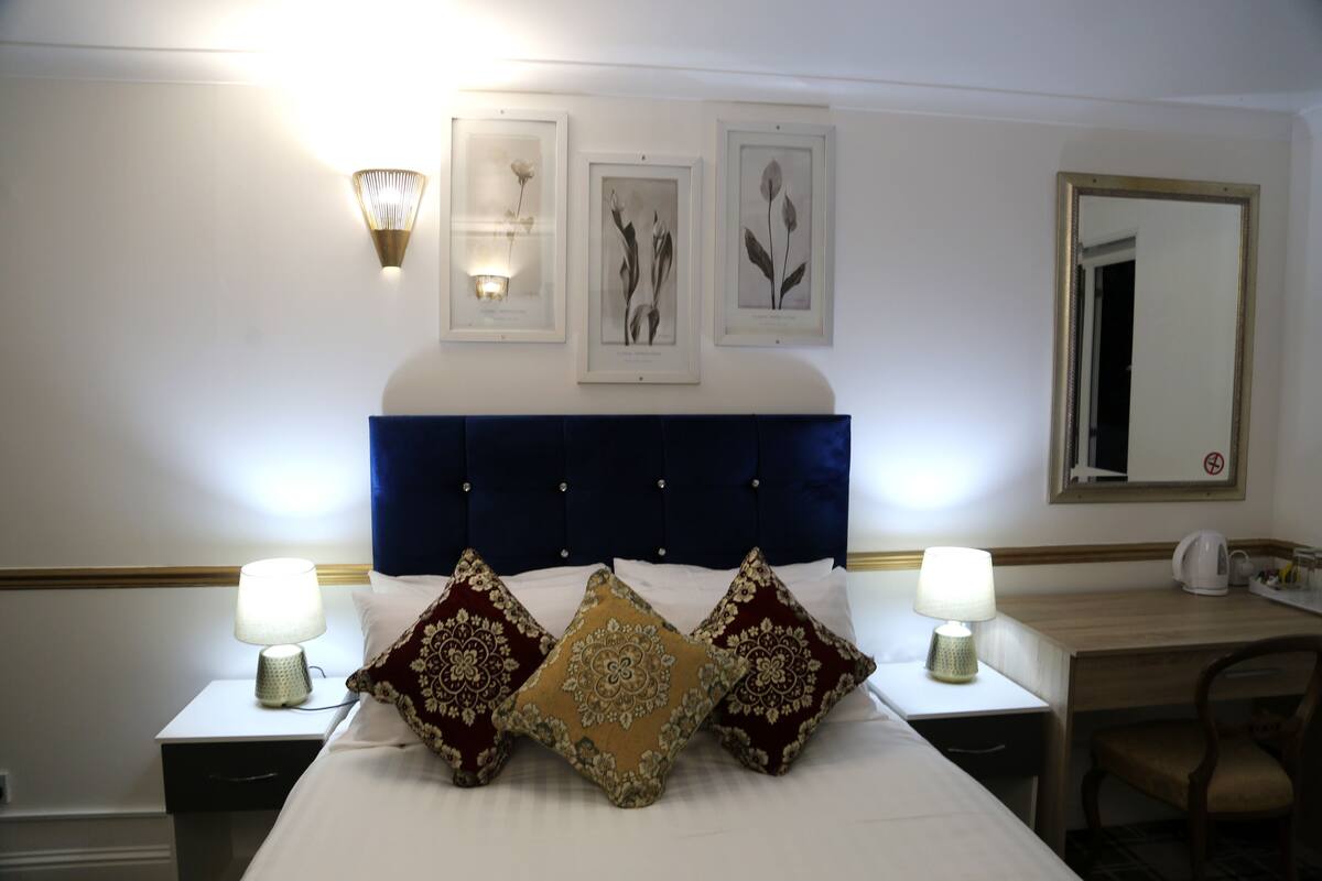 A hotel room with a large bed, two bedside tables with lamps, a nightstand, a dresser, a chair, and framed botanical prints on the wall.