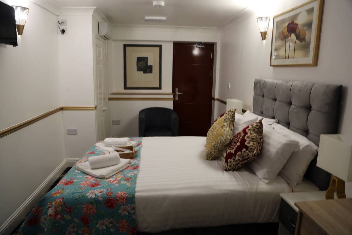 A hotel room with a bed, a chair, a door, and a framed picture on the wall.