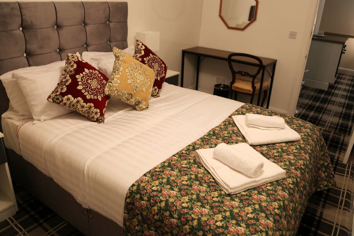 A neatly made bed with floral bedding, a tufted headboard, and two pillows.