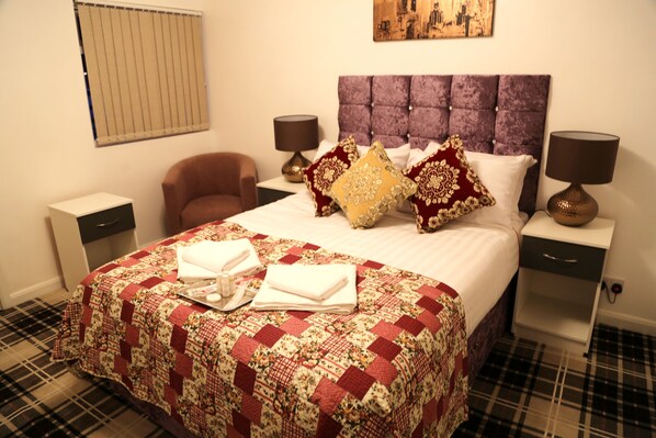 A hotel room with a large bed, two bedside tables, a chair, a window with blinds, and a painting on the wall.