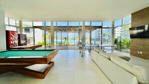 A modern indoor pool area with a pool table, a sofa, and a large window offering a view of the ocean and buildings. - Beach type pool, 10 min from the beach by Gpsrentas (Mazatlán)