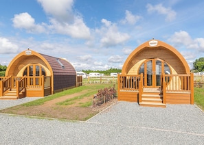 Duas cabanas de madeira com arco, com grades e degraus de madeira, localizadas em um caminho de cascalho com grama entre elas.