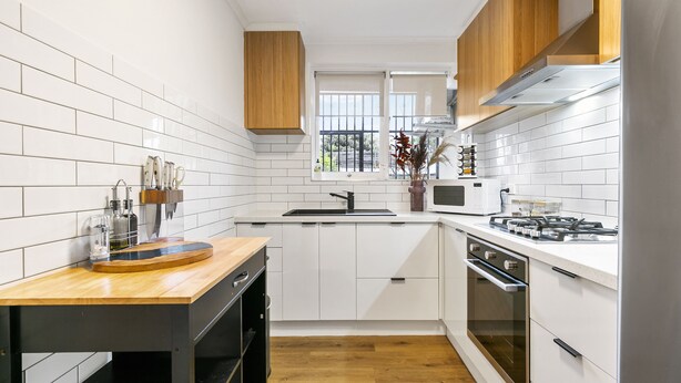 Een moderne keuken met witte kastjes, een houten aanrecht, een gasfornuis en een ingebouwde oven.