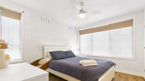 Een slaapkamer met een bed, een bureau, een stoel, een plafondventilator en grote ramen.