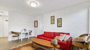 Een woonkamer met een rode bank, een houten salontafel en een eethoek met een witte tafel en stoelen.