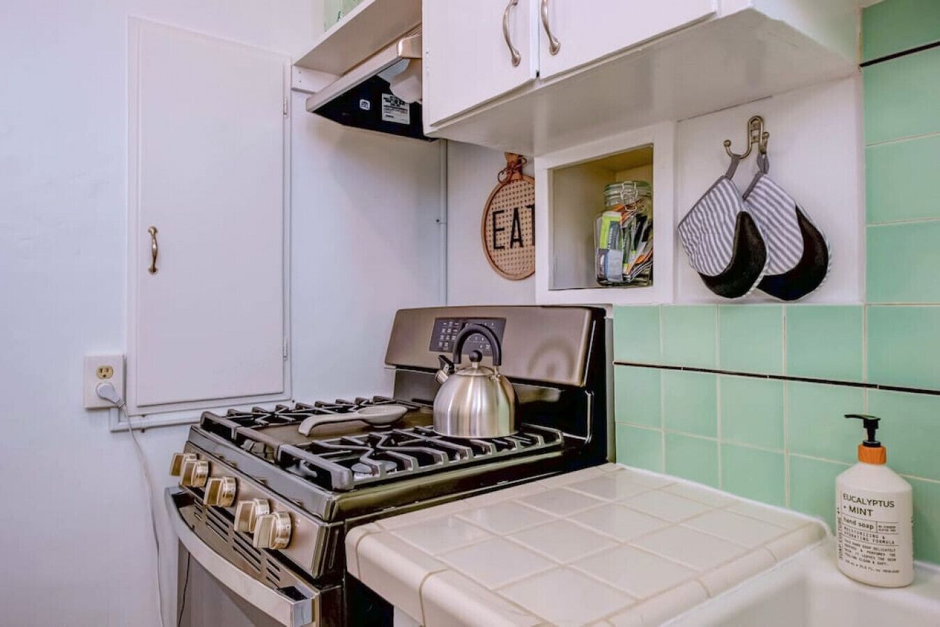 Una cucina con un fornello a gas, un bollitore e una bottiglia di sapone.