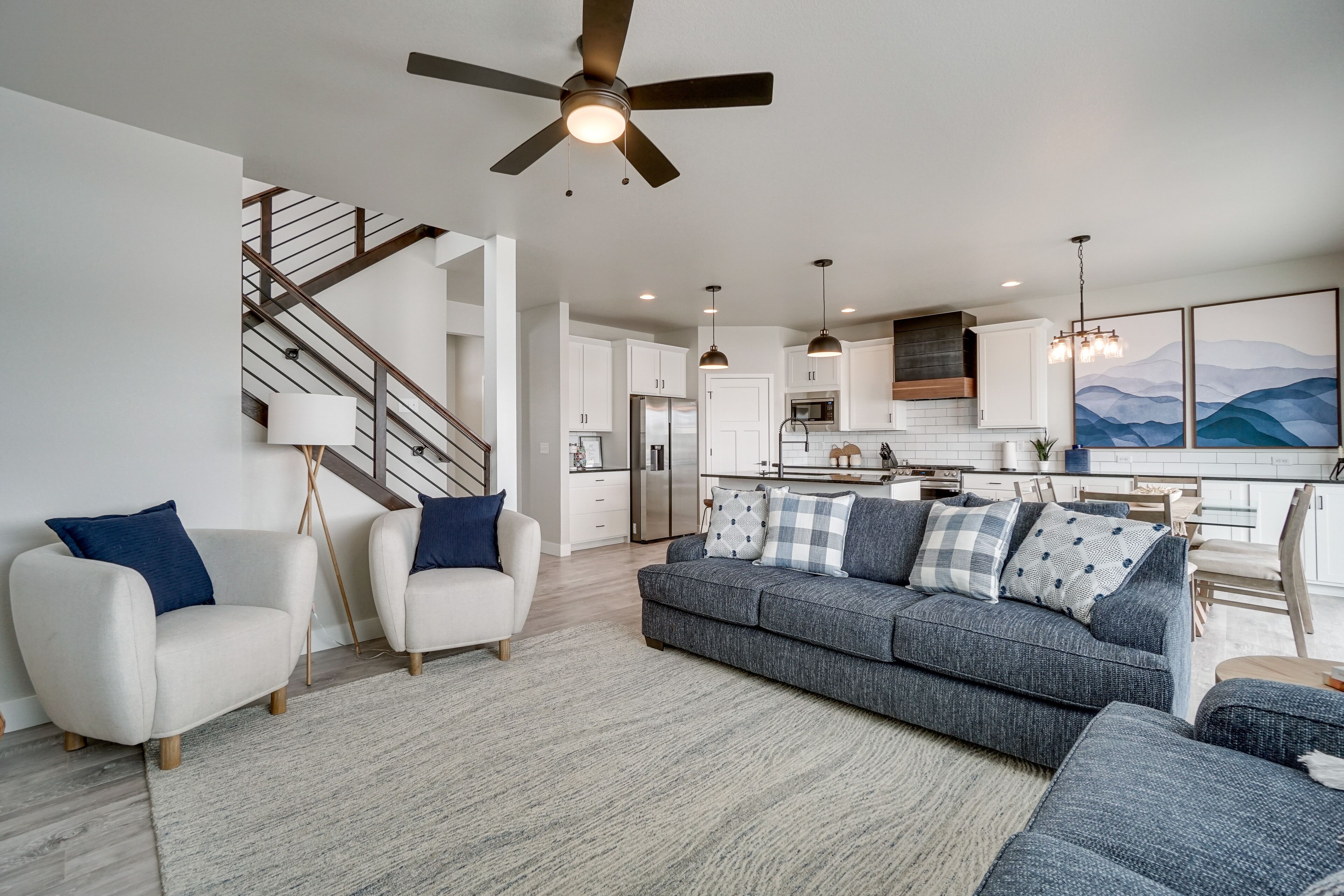 A modern living room with a gray sofa, white armchairs, and a staircase.