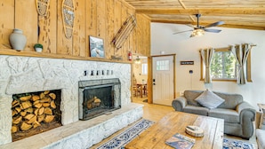 A cozy living room with a stone fireplace, wooden ceiling, and a sofa. - Graeagle Vacation Rental Cabin w/ Game Room! (Graeagle)