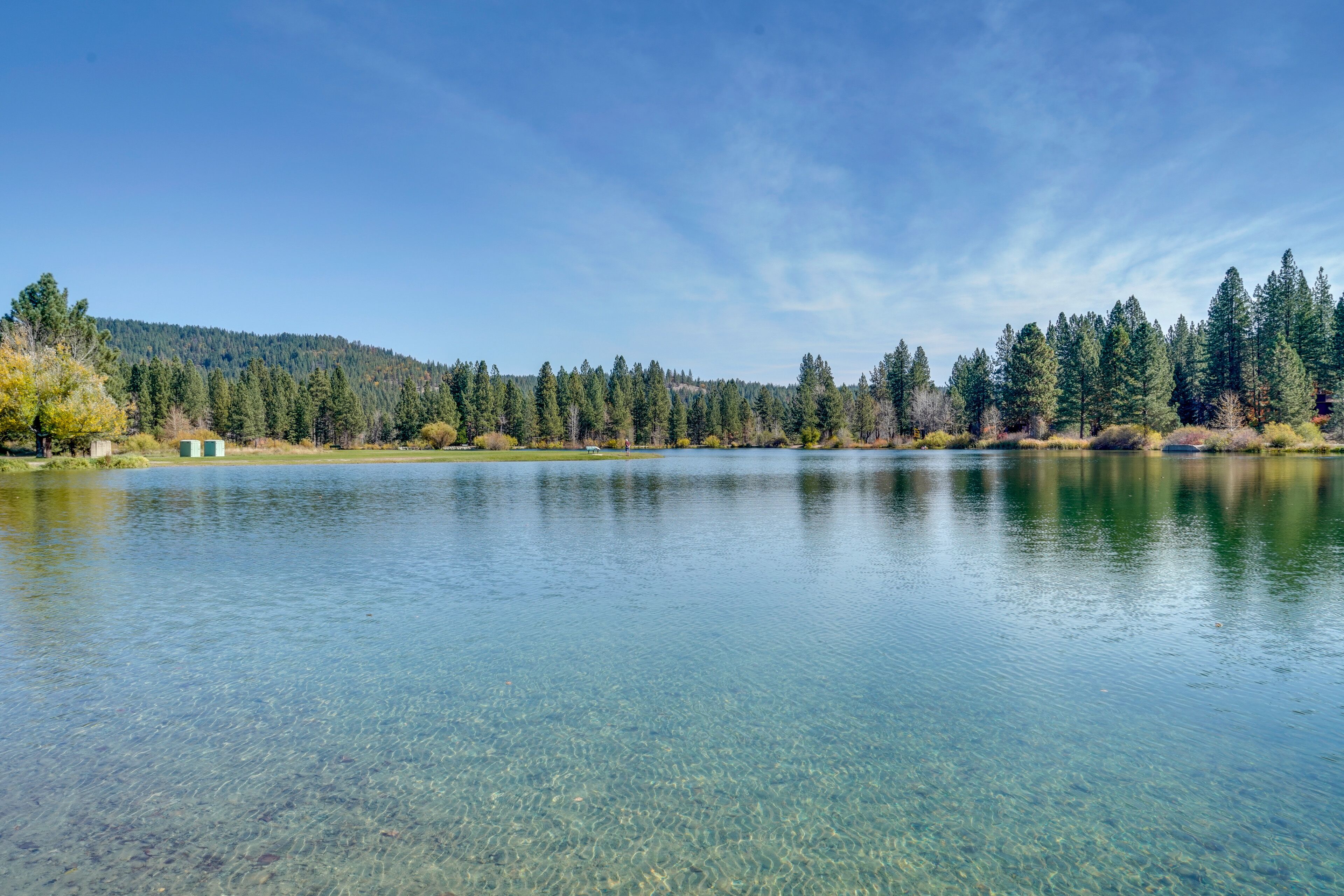A clear lake with a forested hillside in the background.