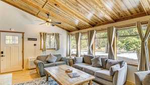 A cozy living room with a wooden ceiling, a sofa set, a coffee table, and large windows with curtains. - Graeagle Vacation Rental Cabin w/ Game Room! (Graeagle)