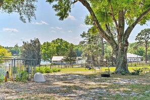 A fenced outdoor area with a large tree, a covered structure, and a small building in the background. - Near Lakes & Parks: Lady Lake Farm Getaway (Lady Lake)