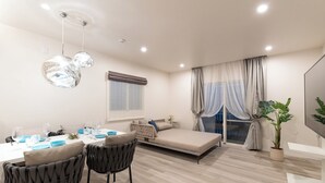 A modern living room with a dining area, a sofa bed, and a potted plant. - Crystal Villa Ikema (Miyakojima)