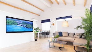 A modern living room with a large flat-screen TV, a sofa, a coffee table, and a dining area with chairs and a table. - Crystal Villa Ikema (Miyakojima)