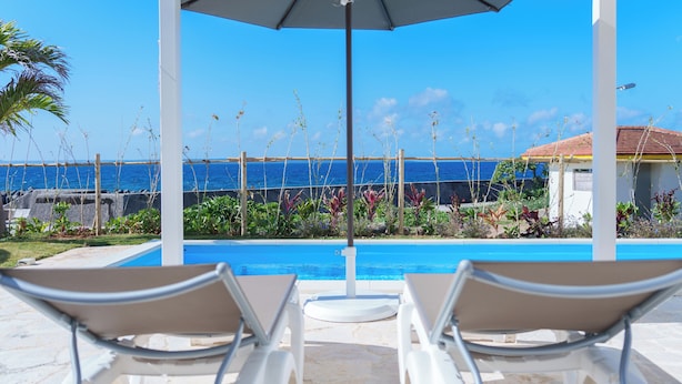 A poolside area with lounge chairs and an umbrella, overlooking a clear blue pool and ocean view. - Crystal Villa Ikema (Miyakojima)
