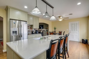 A modern kitchen with a central island, stainless steel appliances, pendant lighting, and a dining area with chairs.