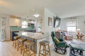Une cuisine moderne avec un îlot central, des tabourets de bar, un fauteuil à bascule vert et une vue sur l’espace de vie.
