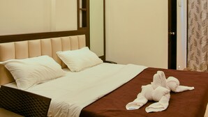 A neatly made bed with a brown bedspread and white pillows, a wooden headboard, and a bedside table with a lamp. - Malvan's Aishwarya Hotel (Malvan)