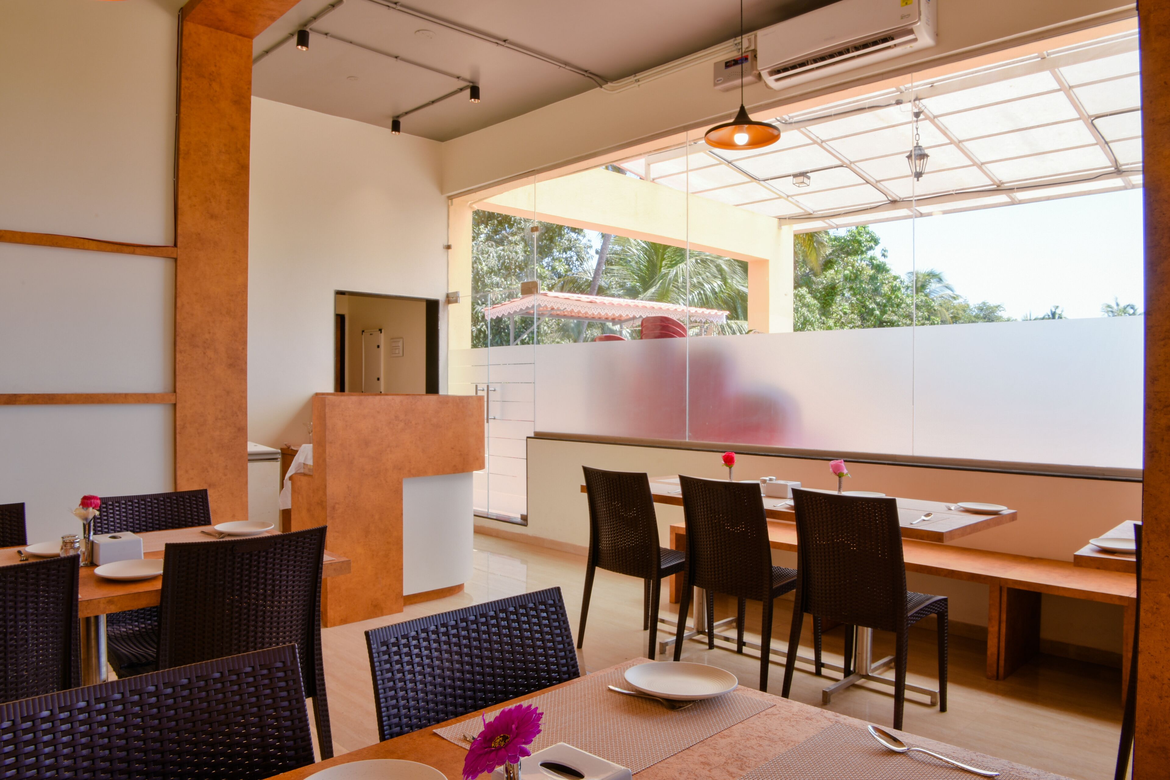 A modern dining area with high tables, dark wicker chairs, and a large window with a view of greenery.