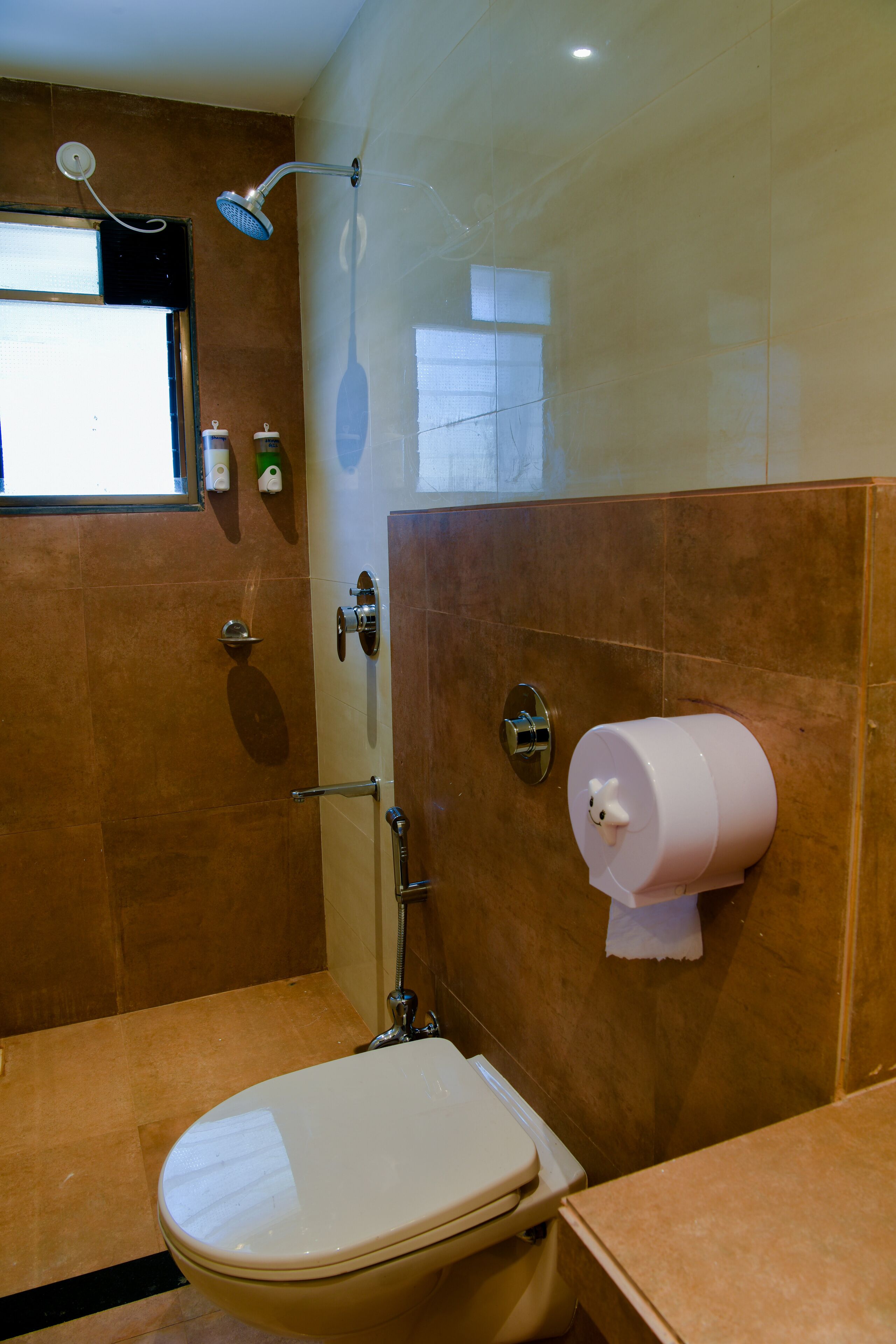 A bathroom with a toilet, a shower, and a towel dispenser.