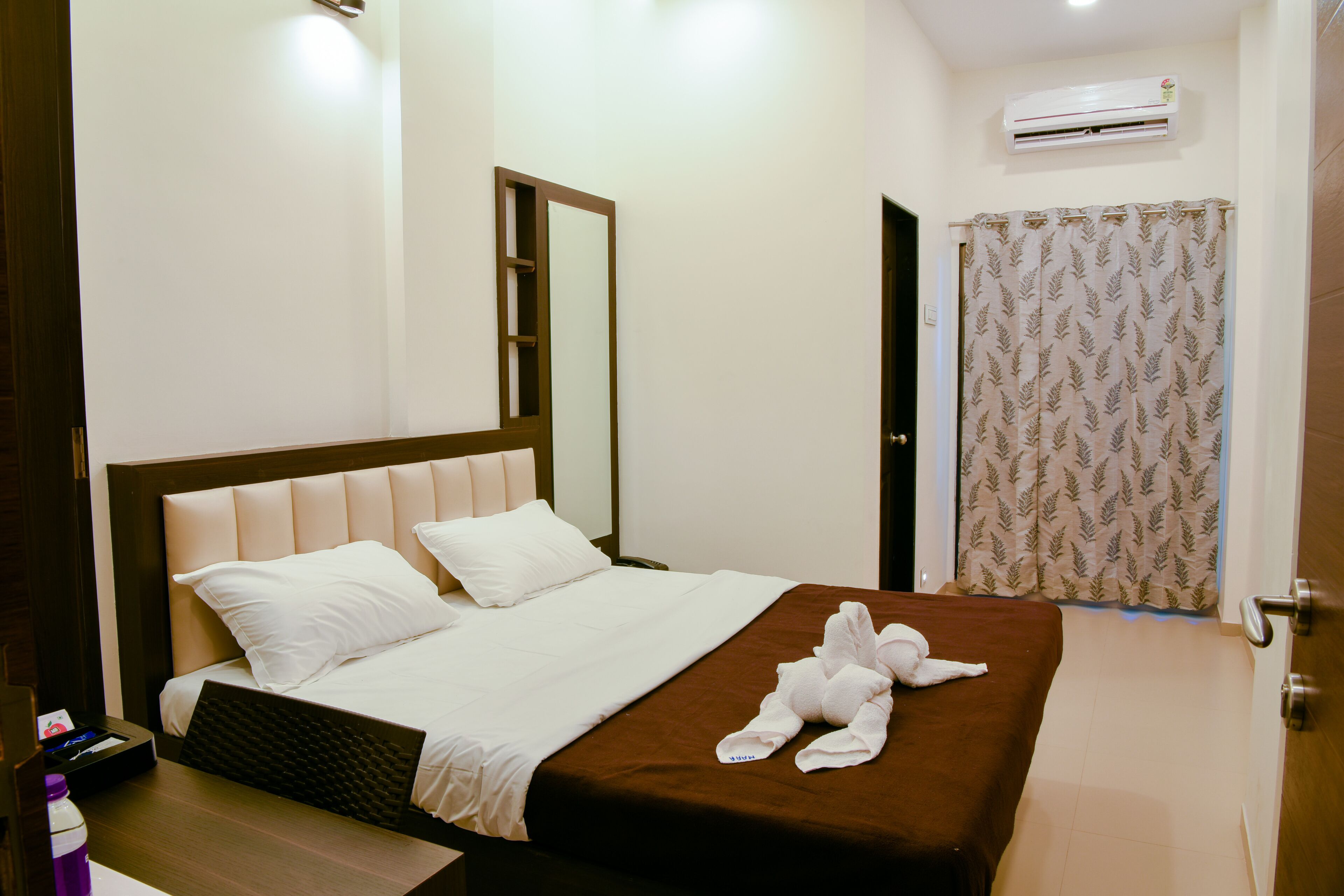 A hotel room with a bed, a bedside table, an air conditioning unit, and a curtain.