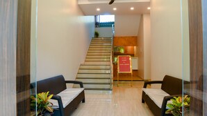 A reception area with a staircase, two sofas, a red welcome sign, and potted plants. - Malvan's Aishwarya Hotel (Malvan)