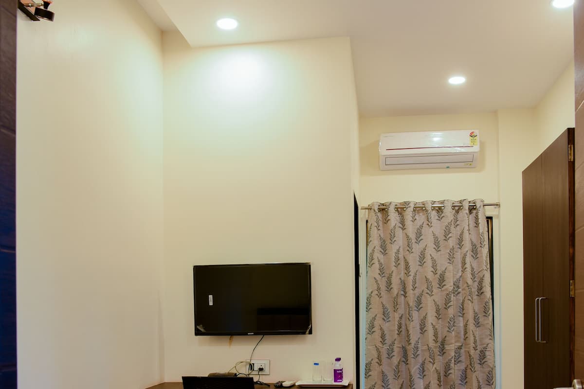 Quarto de hotel com duas camas, uma mesa de trabalho com televisão, ar condicionado e ventoinha no teto.