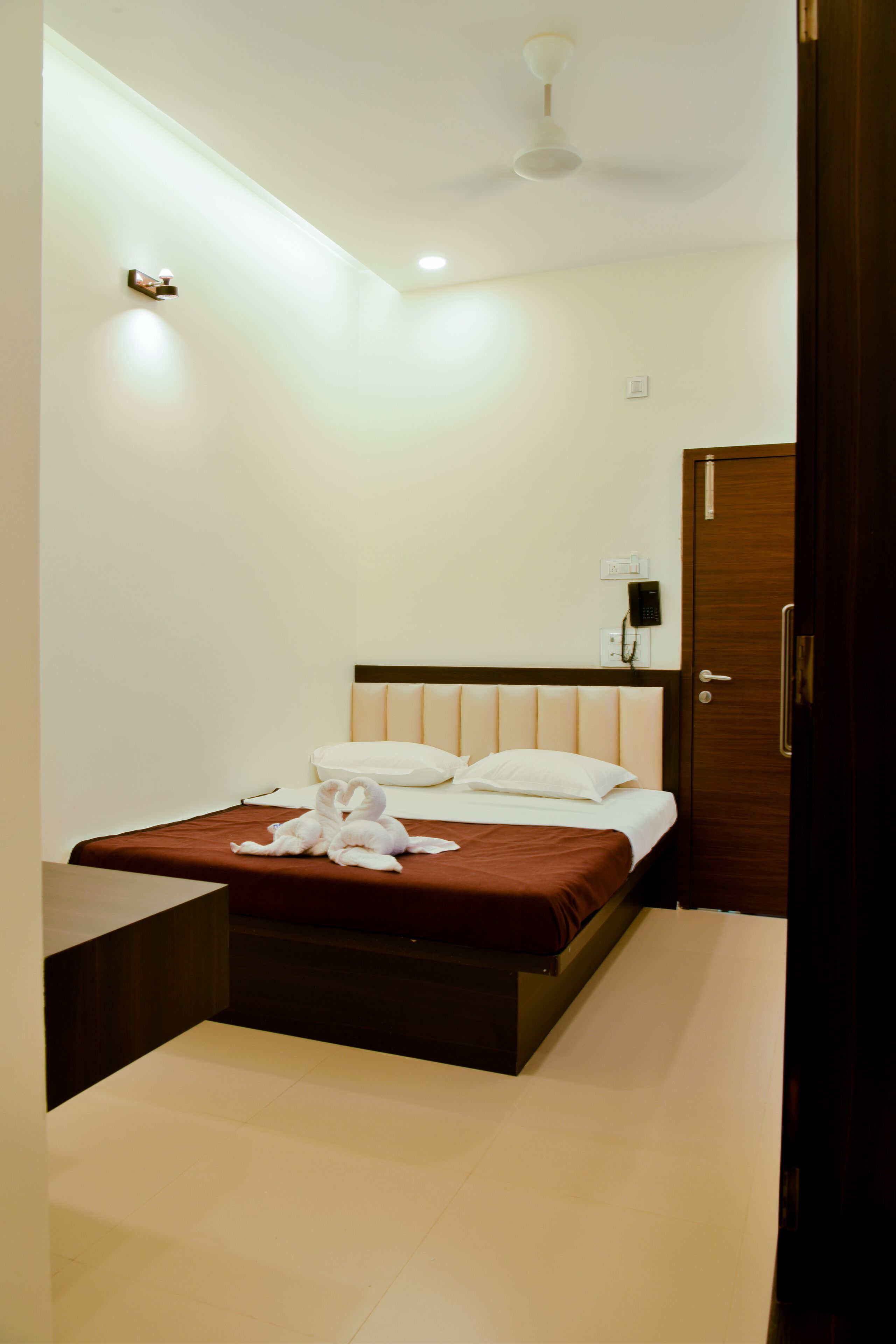 A hotel room with a bed, a bedside table, a ceiling fan, and a door.