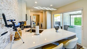 A modern kitchen with a large island, a telescope, and a dining area with chairs. - By Joshua Tree! 'Serenity on Sage' Home w/ Hot Tub (Yucca Valley)