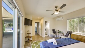 A modern bedroom with a large bed, a ceiling fan, a TV, and a view of the outside. - By Joshua Tree! 'Serenity on Sage' Home w/ Hot Tub (Yucca Valley)