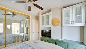Une chambre à coucher avec un lit, un ventilateur de plafond, une télévision et des placards.