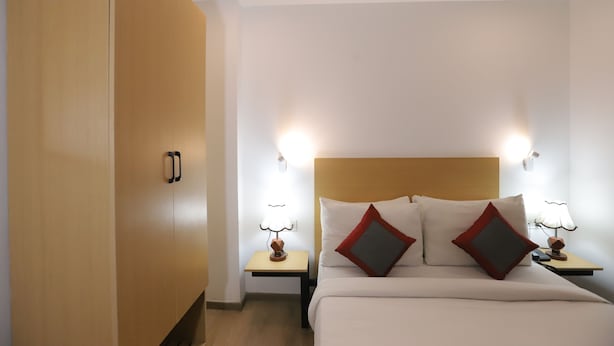 A hotel room with a bed, two bedside tables with lamps, and a wooden wardrobe. - Qotel Hotel La Serene Gagan Vihar (New Delhi)