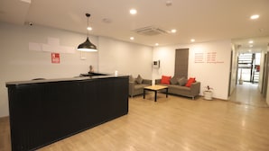 A reception area with a black reception desk, a sofa with red cushions, and a small table. There is a sign indicating the floor levels and a drawing room on the 1st floor. - Qotel Hotel La Serene Gagan Vihar (New Delhi)