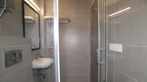 A modern bathroom with a glass shower enclosure, a sink with a mirror above it, and a towel rack. - Qotel Hotel La Serene Gagan Vihar (New Delhi)