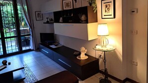 Een moderne woonkamer met een bank, een salontafel en een televisie. Er zijn rekken met decoratieve objecten en een lamp op een bijzettafeltje.