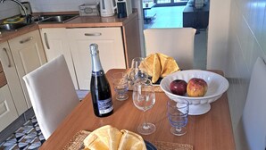 Een eettafel gedekt met een fles, glazen, een fruitschaal en een bord pannenkoeken.