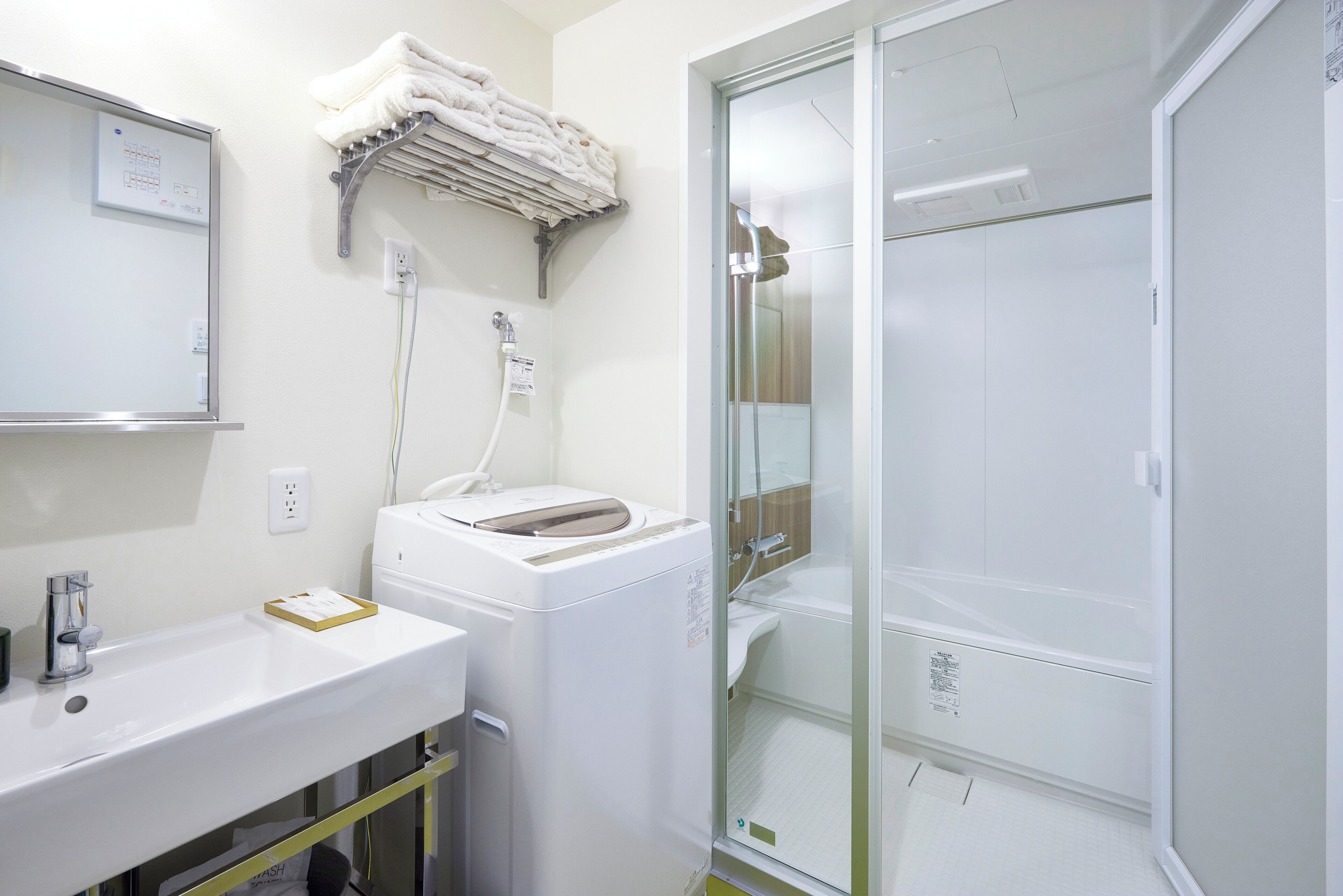 Un baño con lavamanos blanco, lavadora, cabina de ducha de cristal y un perchero para toallas.